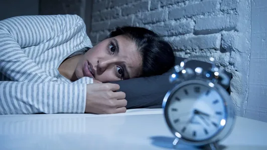 Mulher deitada na cama, acordada, olhando para o despertador
